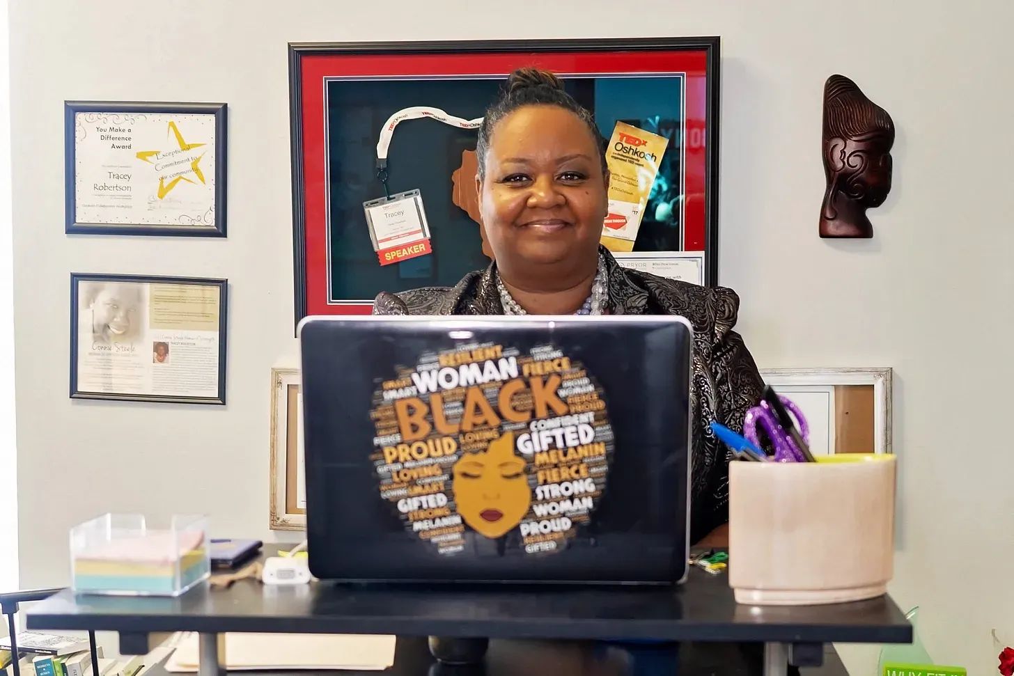 A woman at a standing desk with a laptop computer in the foreground with a sticker on it saying things like "black" and "woman" and "gifted"
